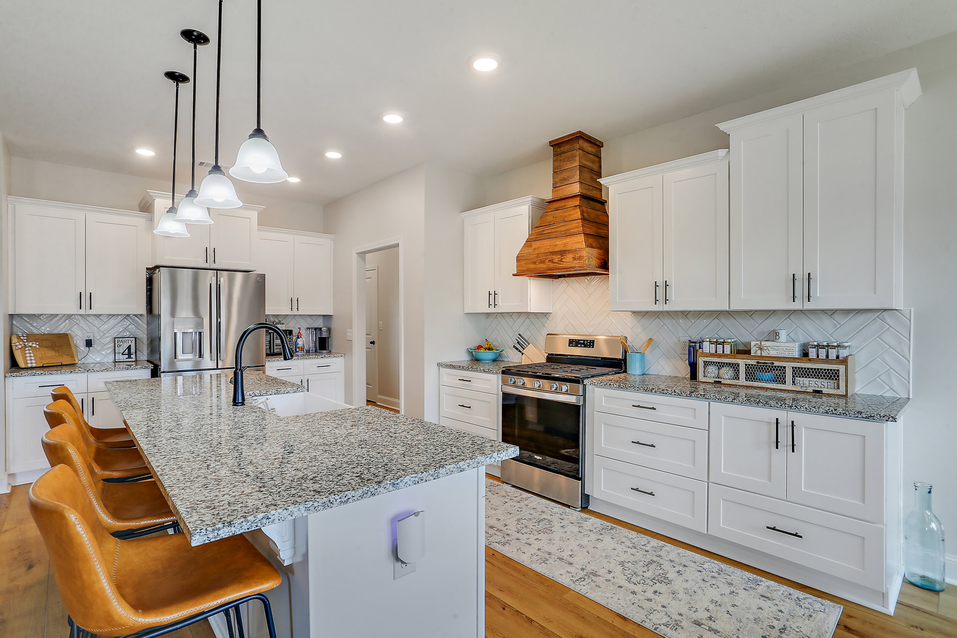 White kitchen cabinets with granite countertops, stainless steel refrigerator, black faucet at the sink, stove, dining table with chairs, black pendant lamp above the kitchen