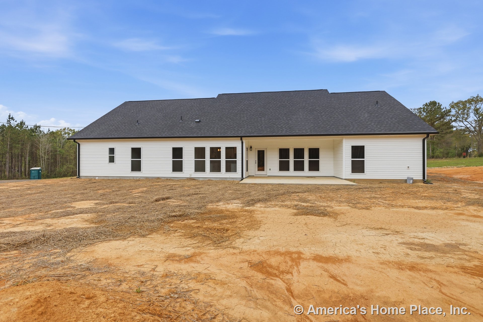 Two-story house with expansive black roof, white-framed windows, and dirt patch yard under cloudy sky