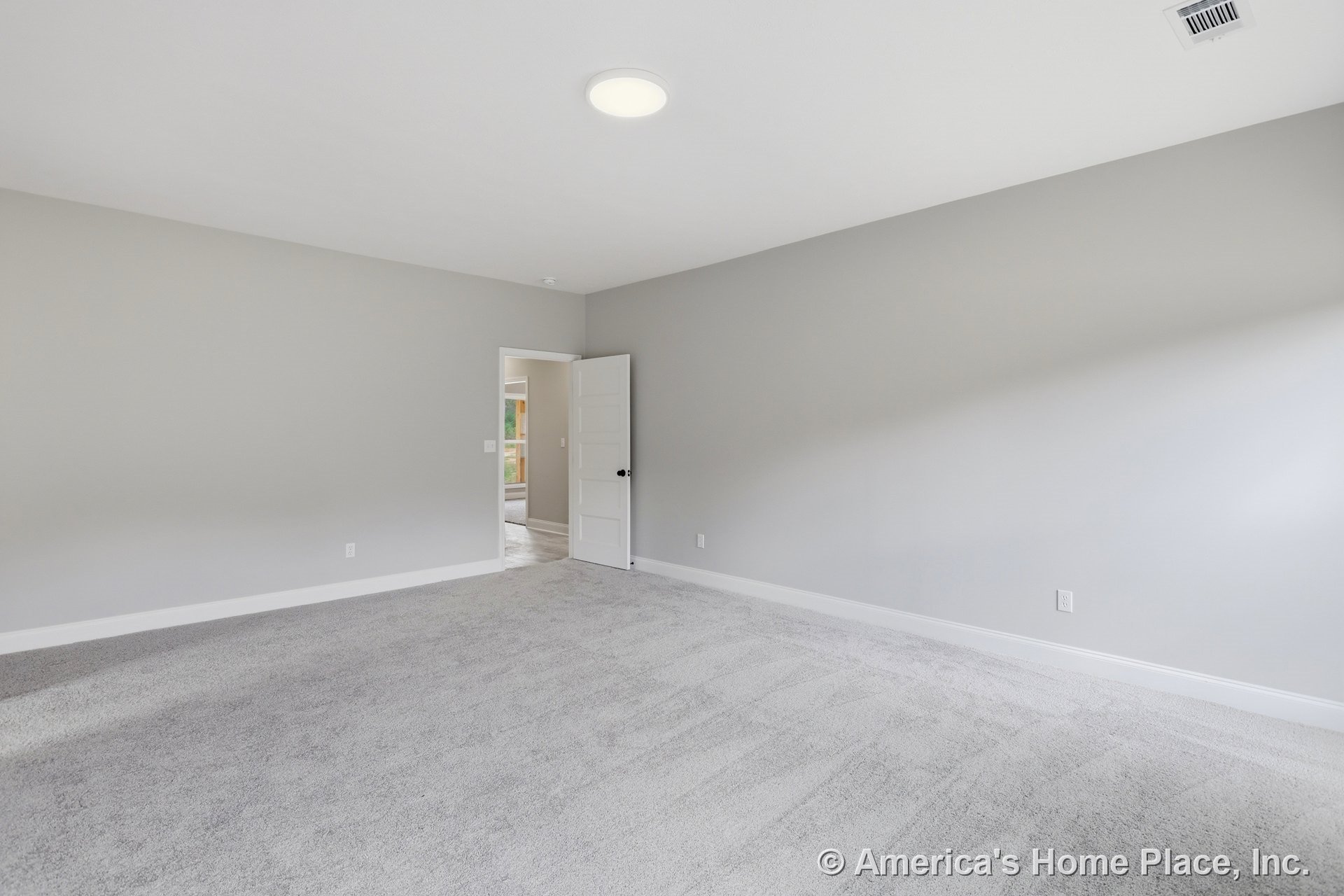 White carpeted room with white walls, white ceiling featuring recessed light and ceiling vent, and an open white door with a black knob leading to another room.