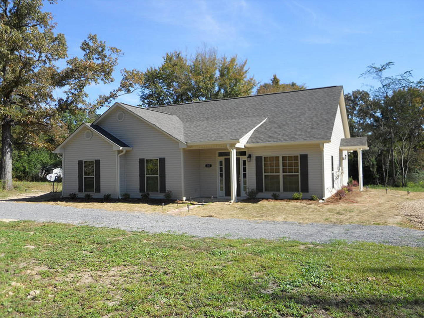 Two-story home with white-framed windows, covered front porch, gray shingle roof, gravel driveway, and manicured grass lawn