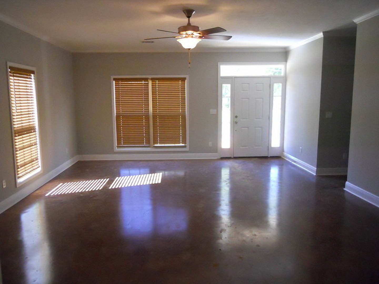 Living room with wood laminate flooring, ceiling fan with light fixture, large window, white door with silver handle and glass panes, neutral walls and ceiling
