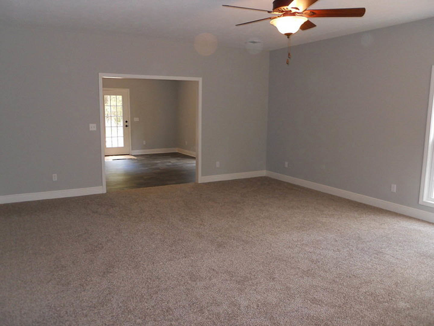 Carpeted bedroom with white walls, ceiling fan with light fixture, open white door, and baseboard trim