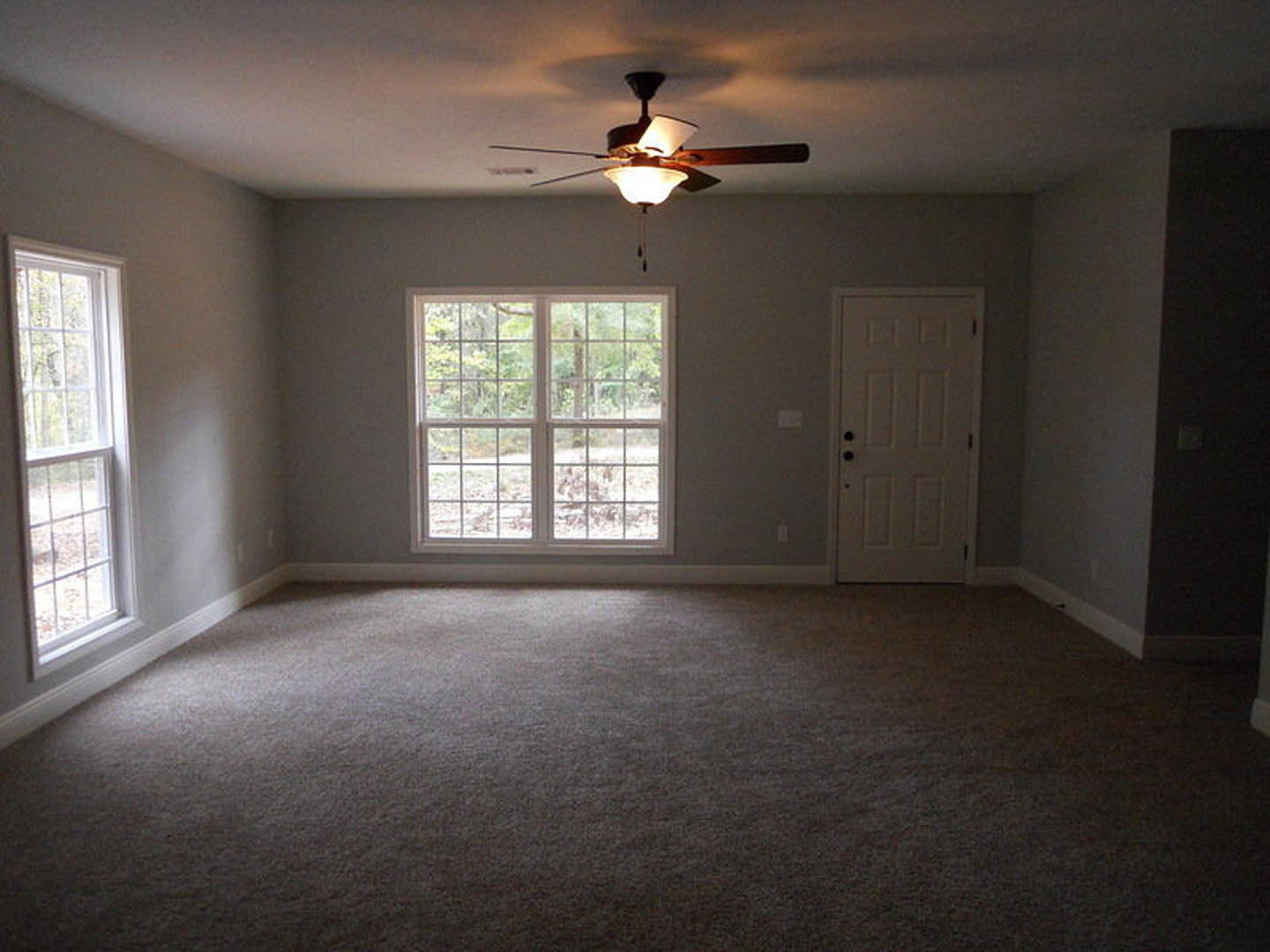 Ceiling fan with light fixture, multi-pane window with white trim, white door with black hardware, neutral walls and flooring in a residential room