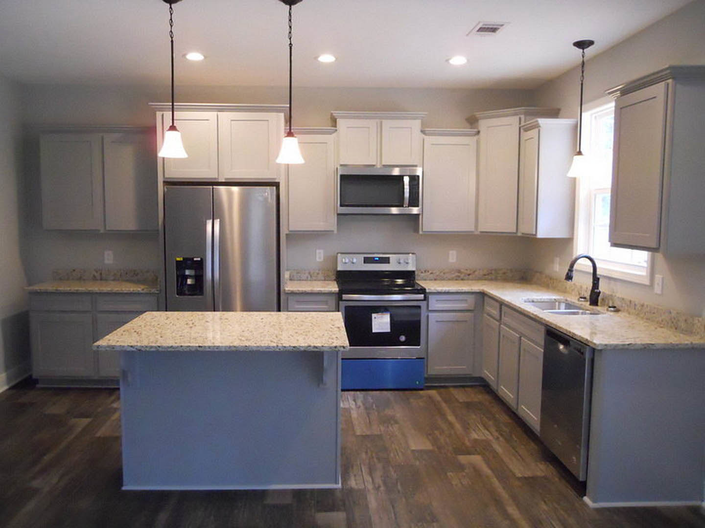 Kitchen with a large central island, stainless steel refrigerator, stove, and microwave, white cabinetry, tile backsplash, and stone countertops