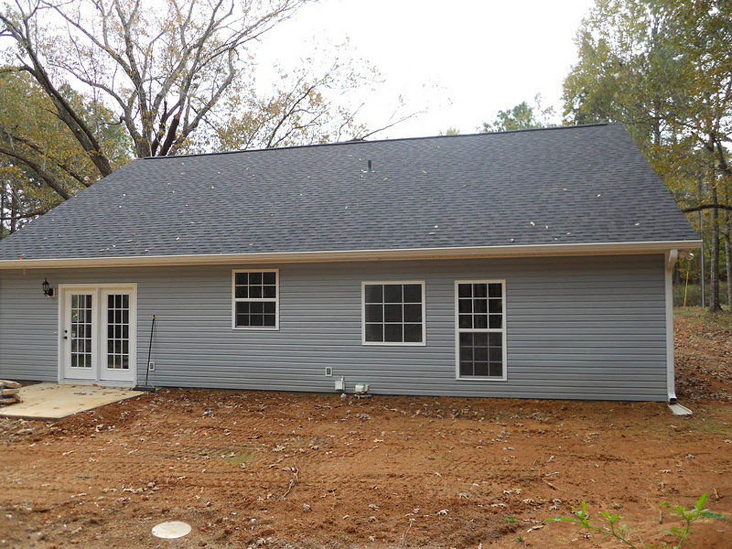 Two-story house with light-colored siding, attached garage, multiple white-framed windows with glass panes, white double entry doors, and a circular feature on the driveway.