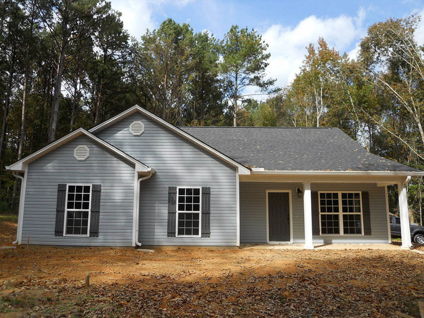 Two-story home with grey roof, white siding, multi-pane windows, and white vent; surrounded by mature trees and cloudy sky in background