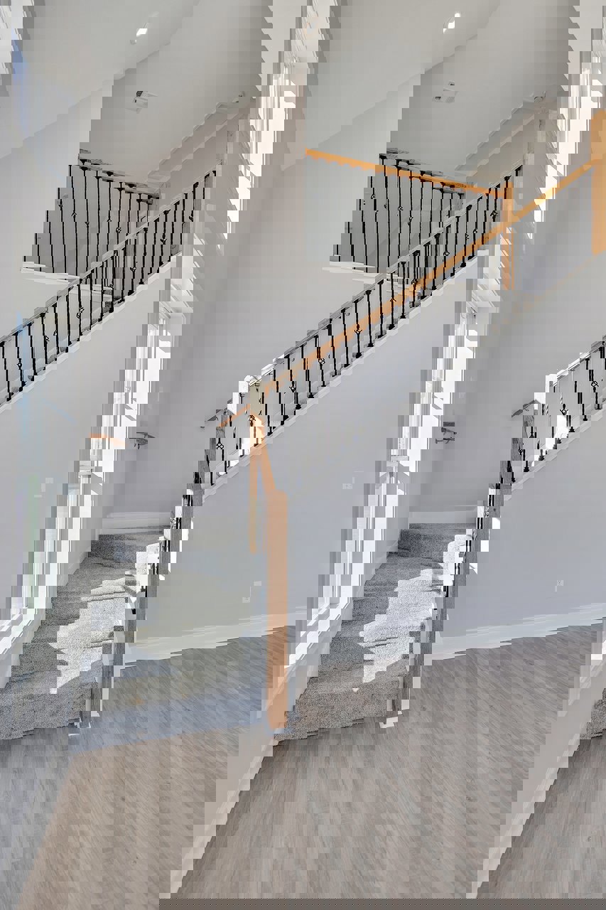 Wood staircase with black metal railings, laminate flooring, white walls, and a window letting in natural light