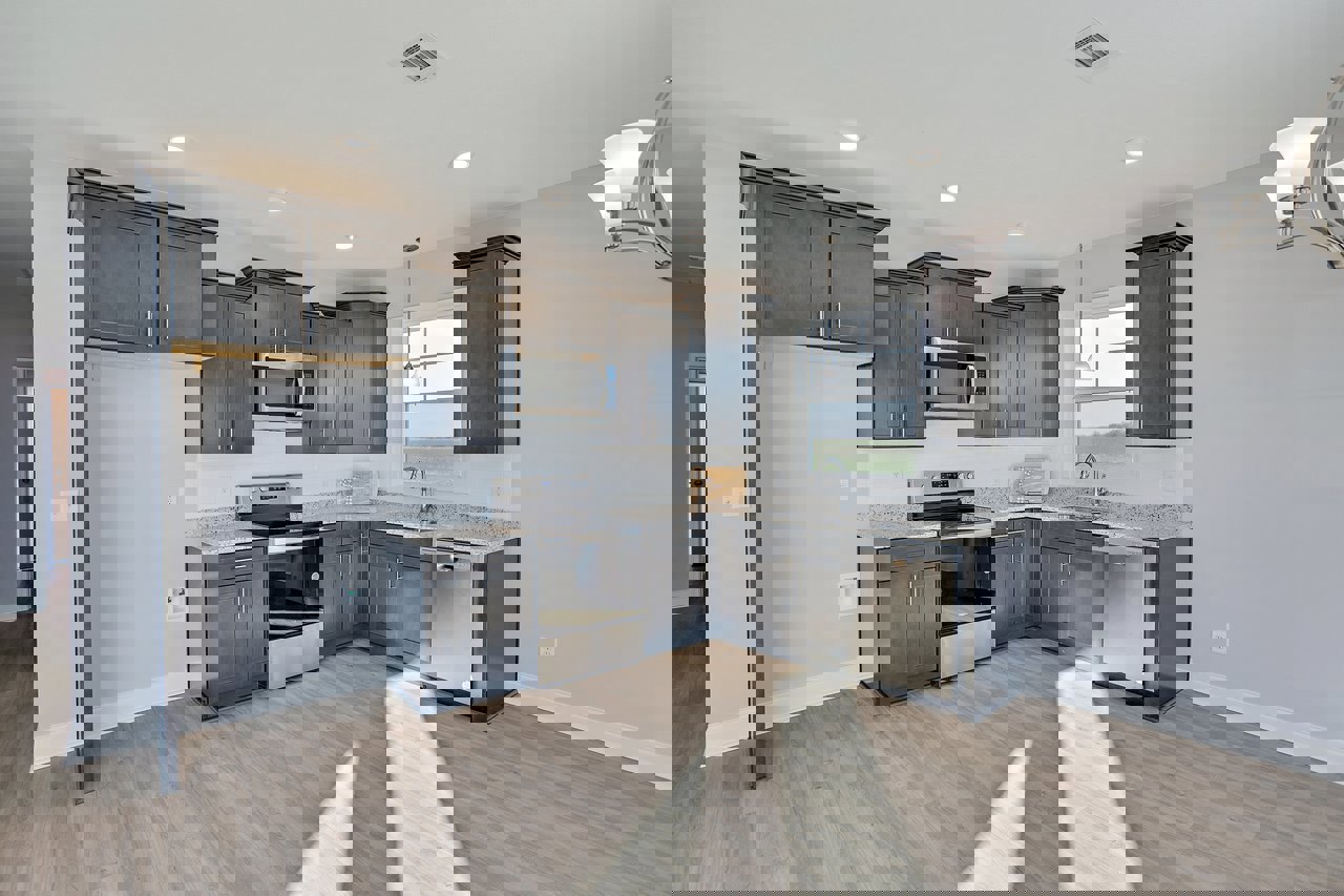 Black kitchen cabinets with brushed metal hardware, wood plank flooring, stainless steel appliances including an open microwave and illuminated dishwasher, white walls, modern