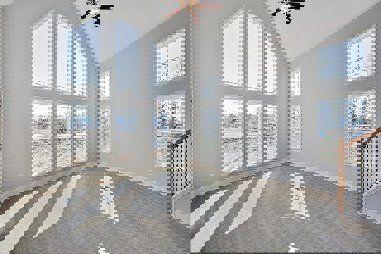 Spacious room featuring multiple large windows, wood flooring, white square tile accent, ceiling fan with light, and close-up view of wooden staircase.