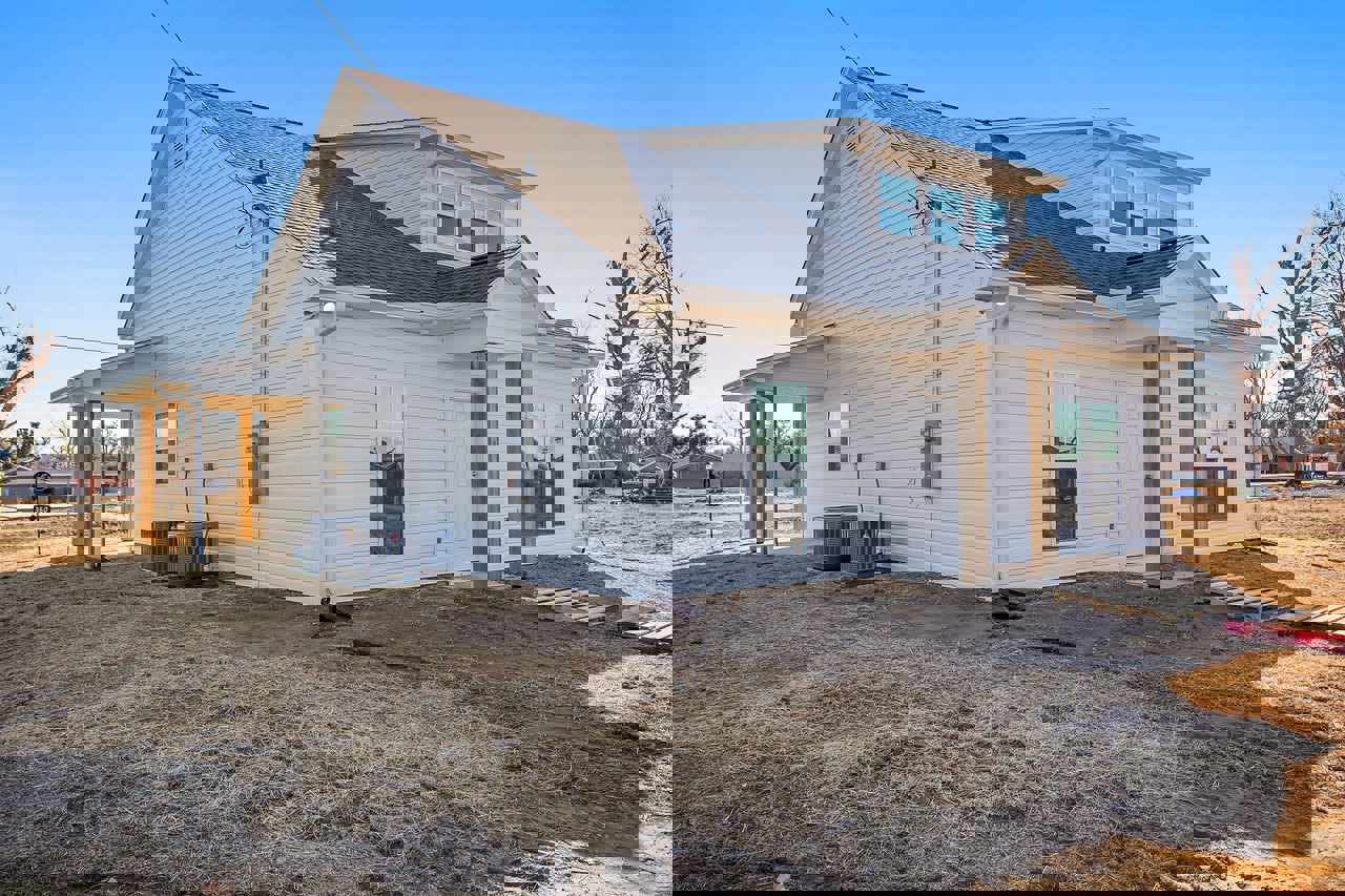 White siding house with white-framed windows, unfinished yard with patchy grass, leafless tree, and black container on a truck in driveway