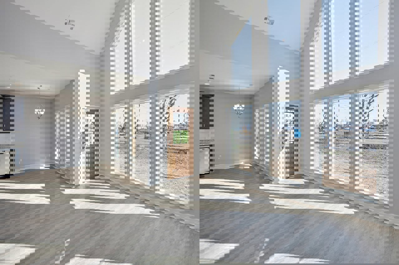 Spacious room featuring expansive windows, wooden flooring illuminated by overhead chandelier with white shades, black cabinet with white trim, and door with glass panel