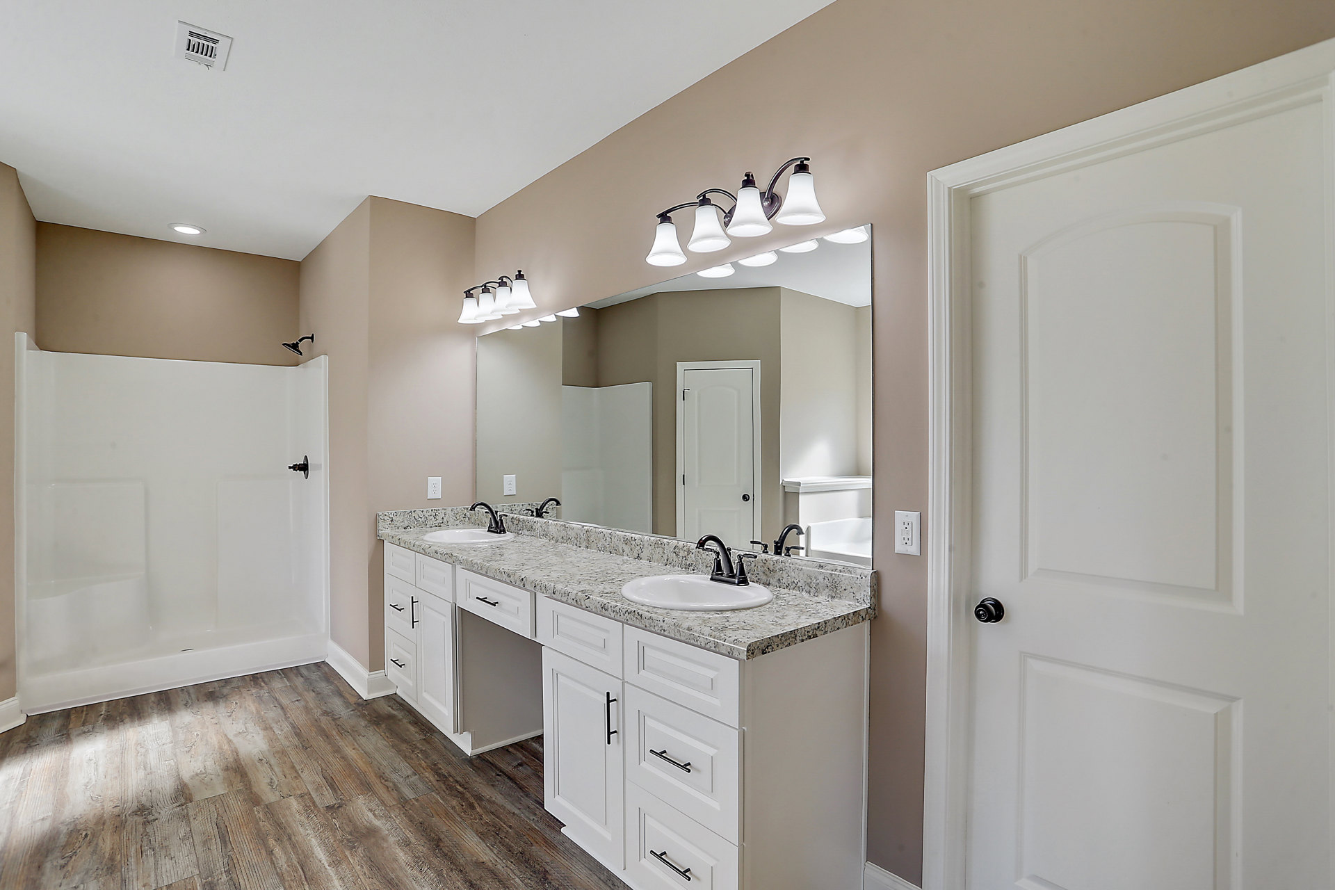 Bathroom featuring double vanity with white sinks, large framed mirror, tiled walls, modern light fixtures, white shower enclosure, and white door with black handle