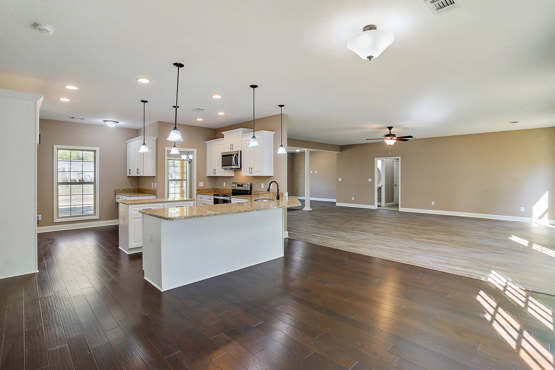 Open-concept kitchen and living room featuring hardwood floors, marble countertop, open microwave, white cabinetry, window overlooking neighboring house, white walls and door