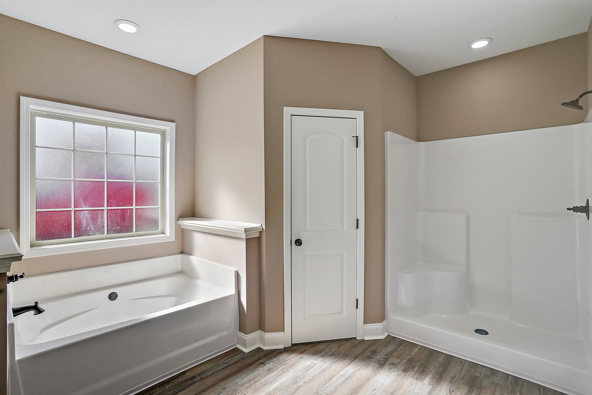 Bathroom with white tile walls, freestanding white bathtub with silver drain, glass shower enclosure, frosted window, white door with black handle, chrome faucet and plumbing