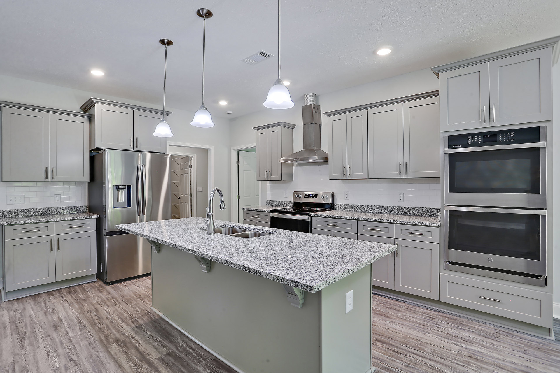 Spacious kitchen featuring a large granite island, stainless steel refrigerator with ice maker, built-in microwave, white cabinetry, and undermount sink