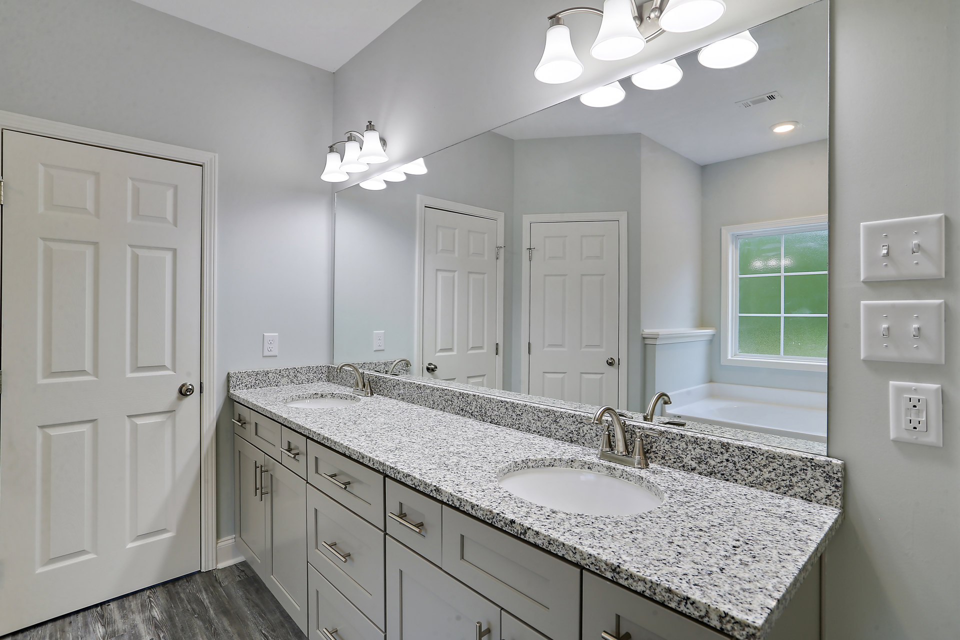 Marble bathroom countertop with white sink featuring black speckled surface, white cabinetry, silver faucet, white door with silver handle, green glass window, and wall outlet