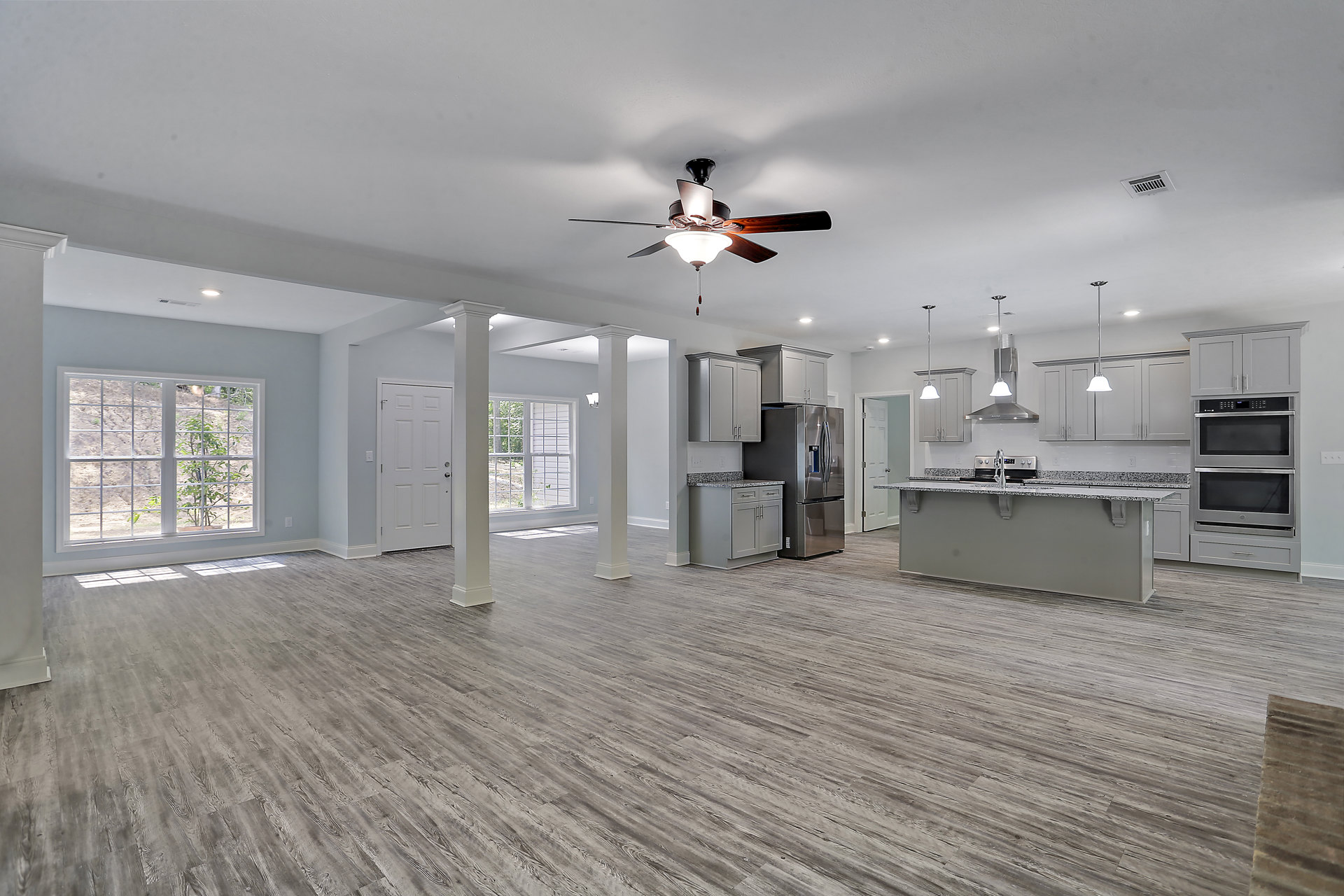 Open floor plan featuring a spacious kitchen with a central island, stainless steel sink and faucet, adjoining living area with ceiling fan and light fixture, large windows