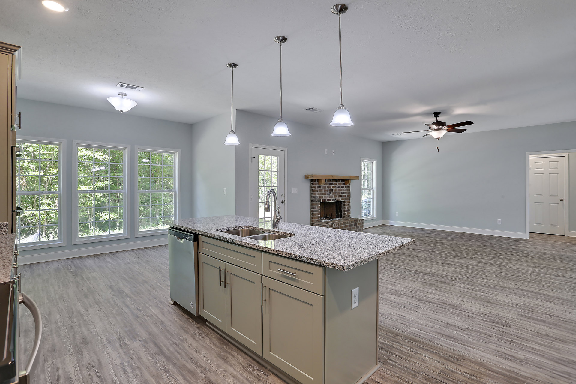 Open-concept kitchen and living room featuring a stone fireplace, white cabinetry, large kitchen island with sink and faucet, hardwood flooring, recessed lighting, and stainless