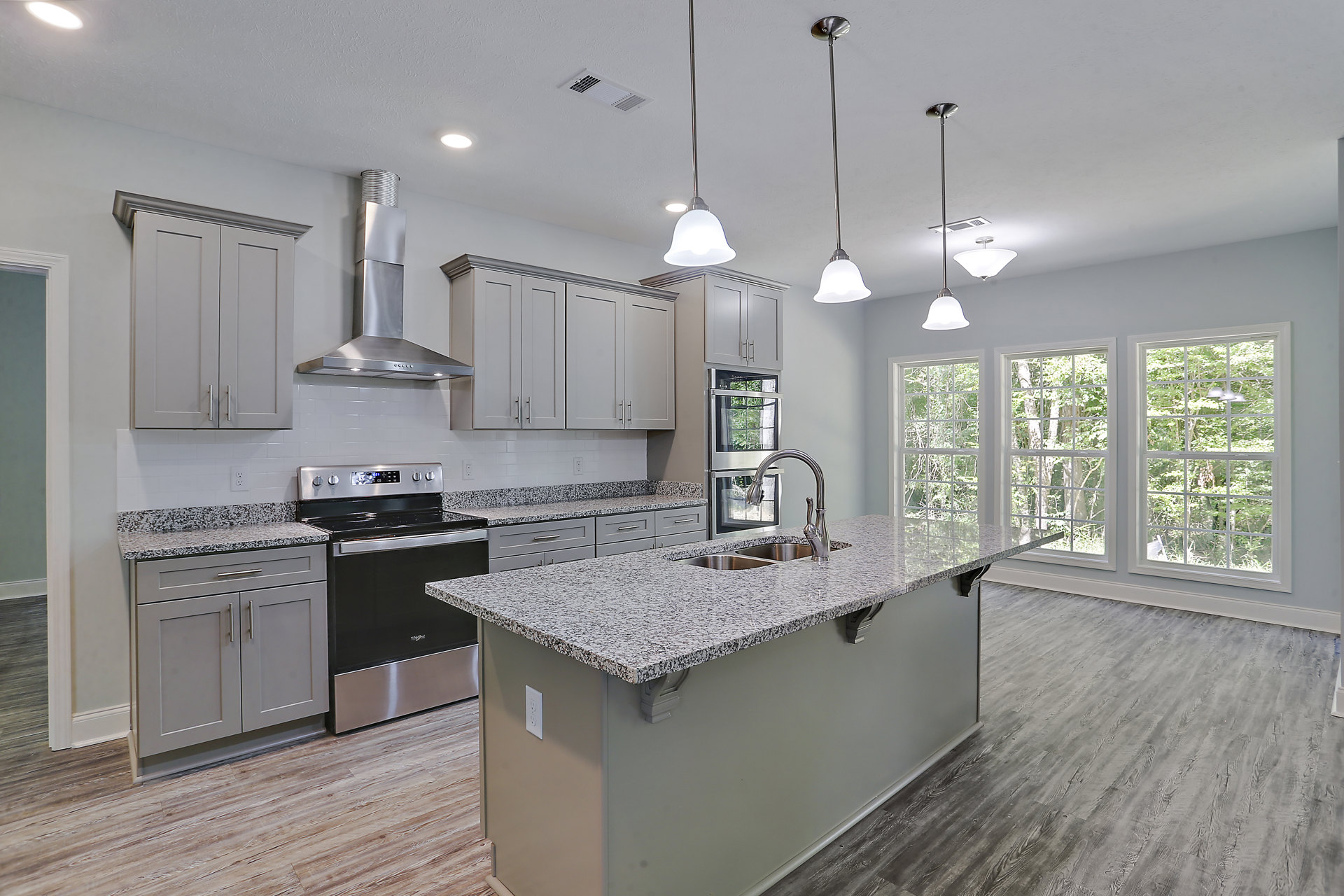 Spacious kitchen featuring a large central island with stone countertop, oversized window, stainless steel sink, black and silver stove, tile backsplash, white cabinetry, and