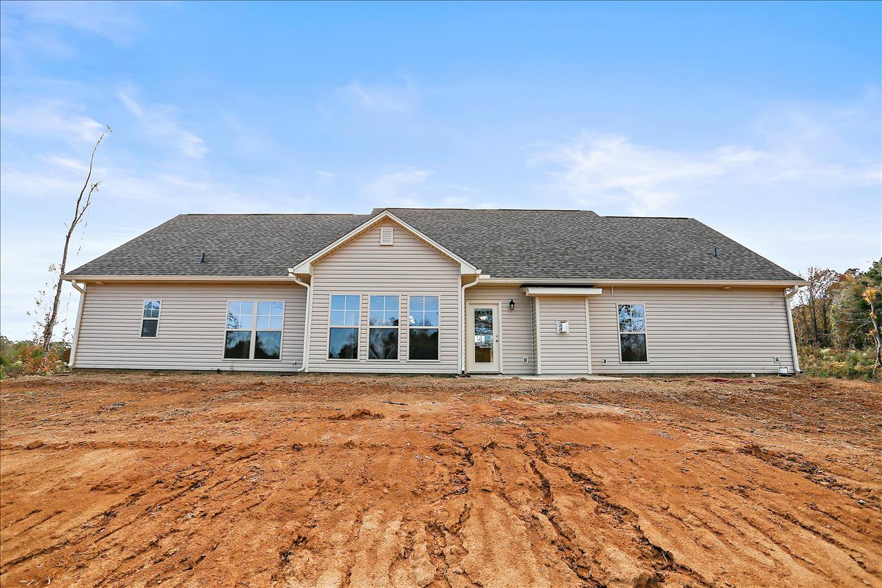 Two-story house with beige siding, several windows, dirt patch in front yard, tree branch overhanging roof, blue sky with scattered clouds