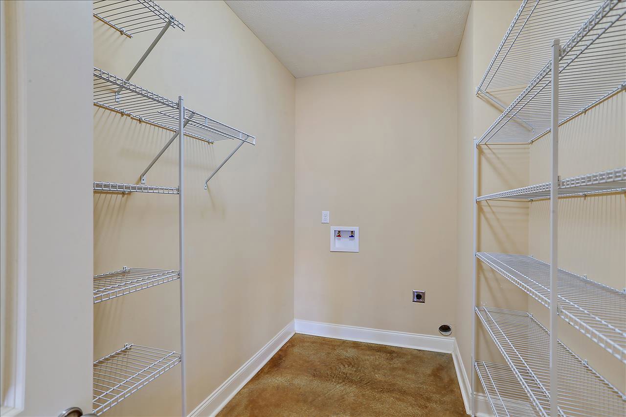 Spacious empty room featuring white built-in shelves on a plaster wall, brown wood flooring with white trim, and a ceiling light fixture; a white storage box with red and blue
