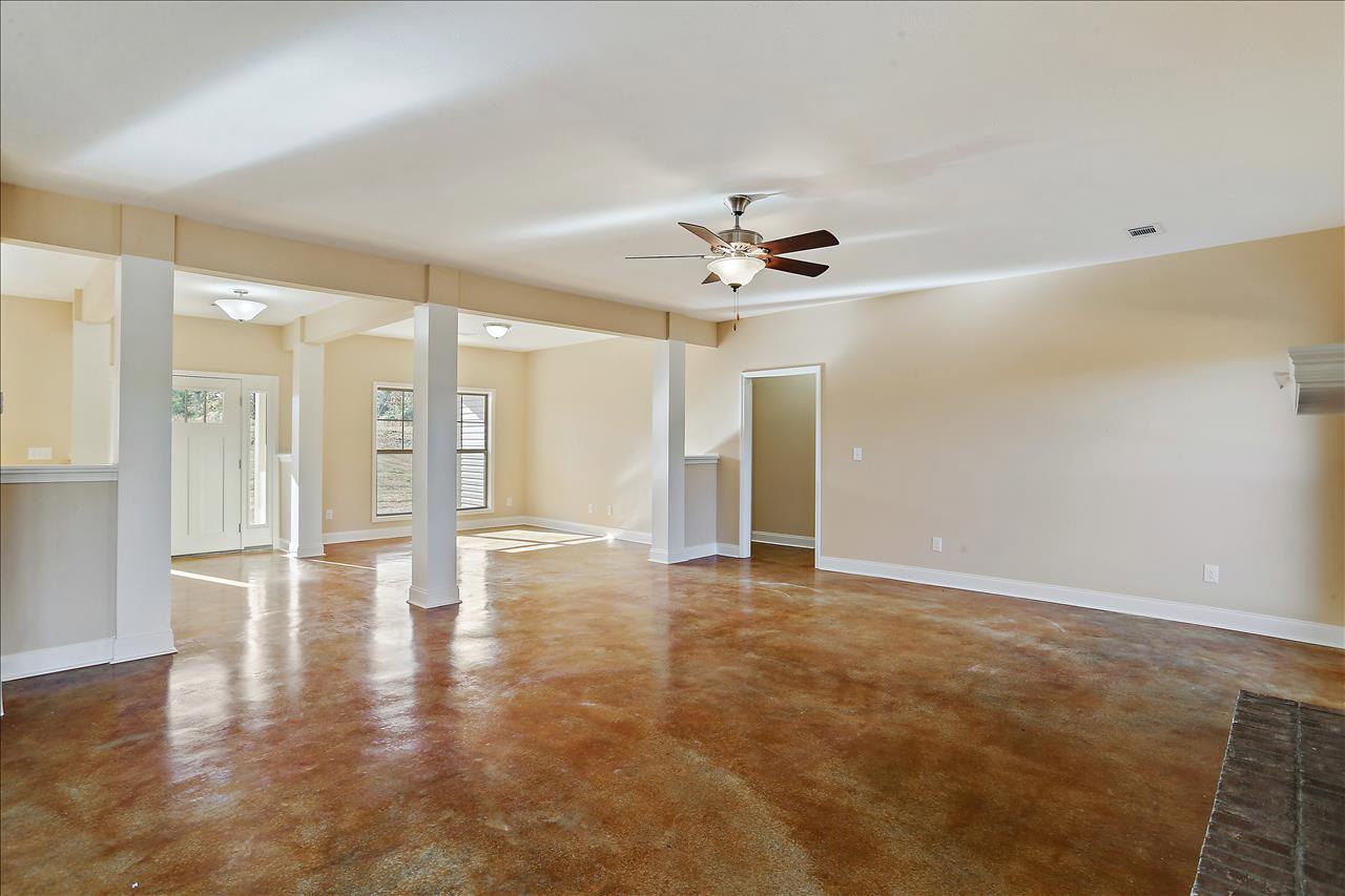 Spacious room featuring wood laminate flooring, white plaster walls, ceiling fan with light fixture, white door with matching trim, exposed brick accent wall, and decorative white