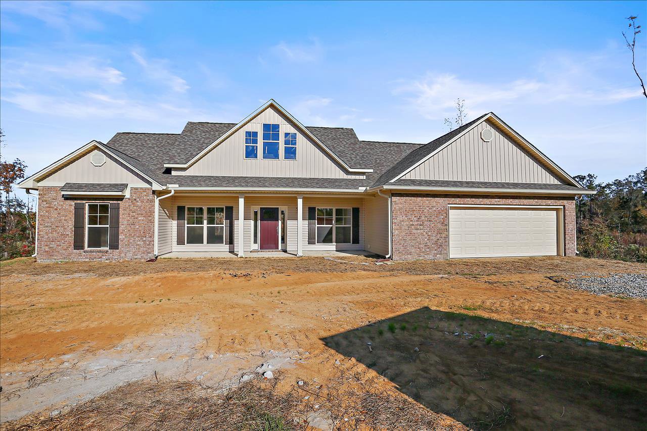 Two-story house with brick roof, white garage door, red front door, and dirt yard with sparse grass patches under a cloudy sky