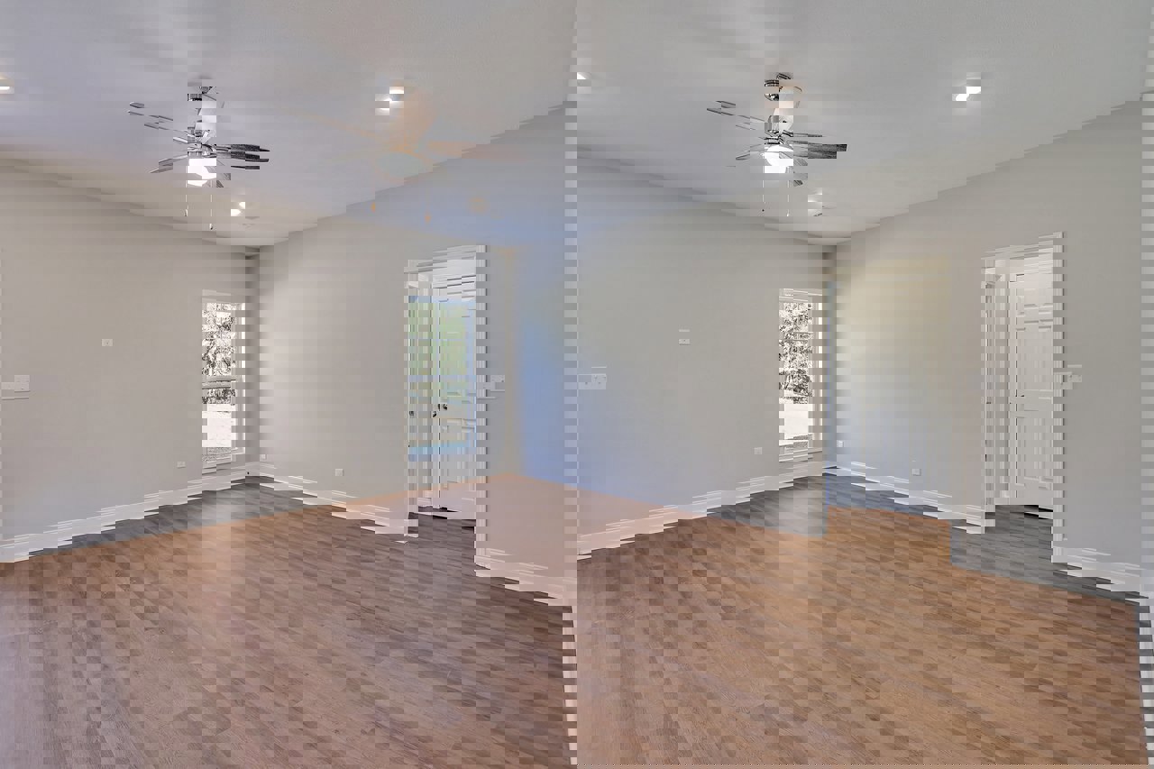 Ceiling fan with light fixture, hardwood floor, white walls, window overlooking trees, white door with silver knobs