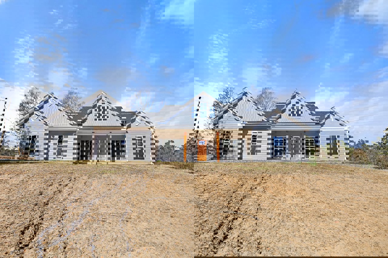 Two-story house with white-framed windows, covered porch, and front door, set against a dirt hill and blue sky
