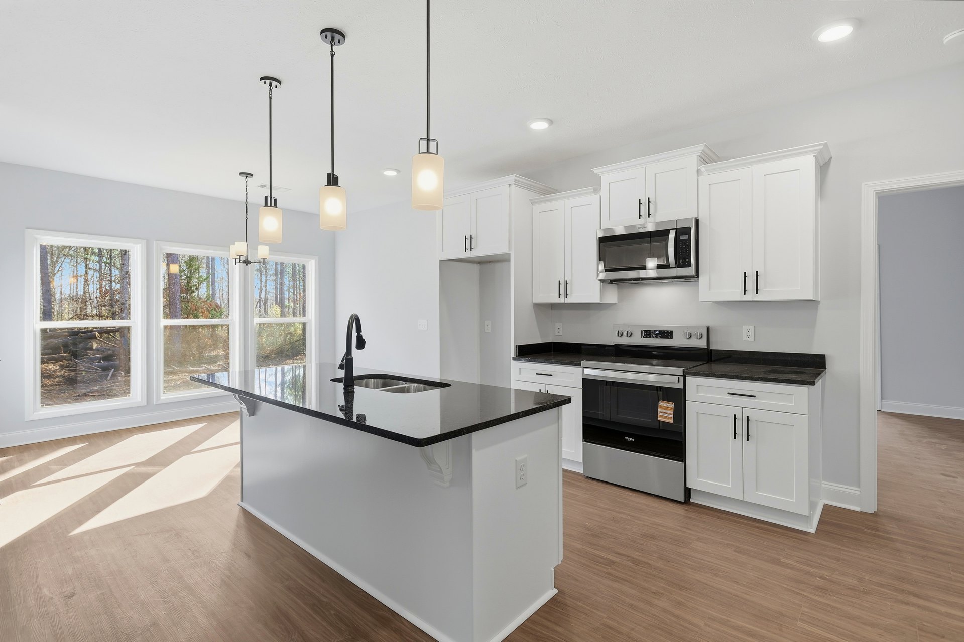White kitchen with black countertops, white cabinetry, kitchen island featuring a built-in sink, stainless steel microwave with illuminated door, close-up of pendant light, black