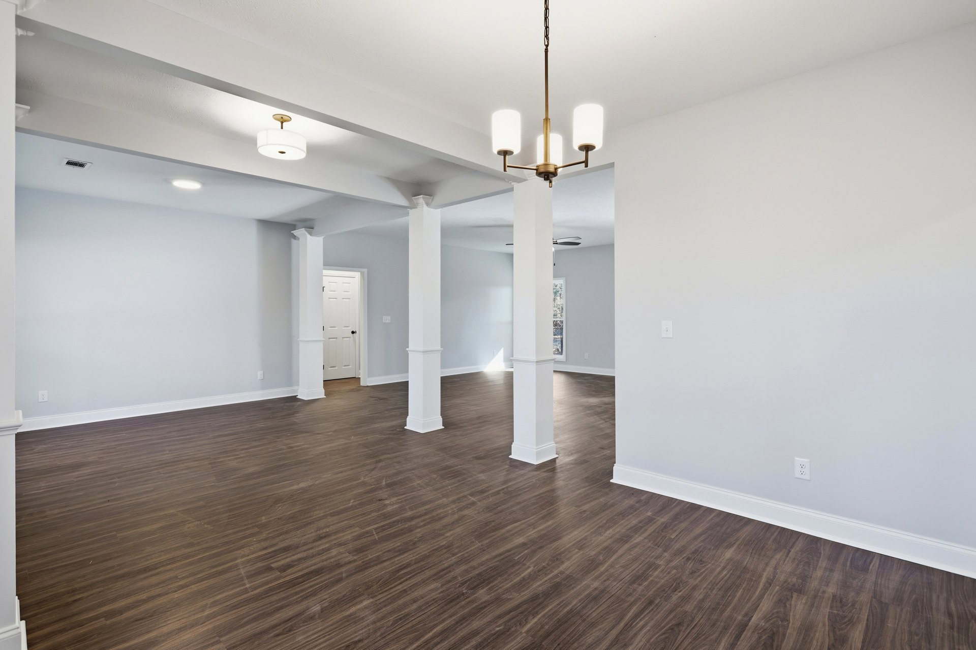 White walls, wood flooring, white pillars, white door with black knob, ceiling-mounted light fixture with white shade