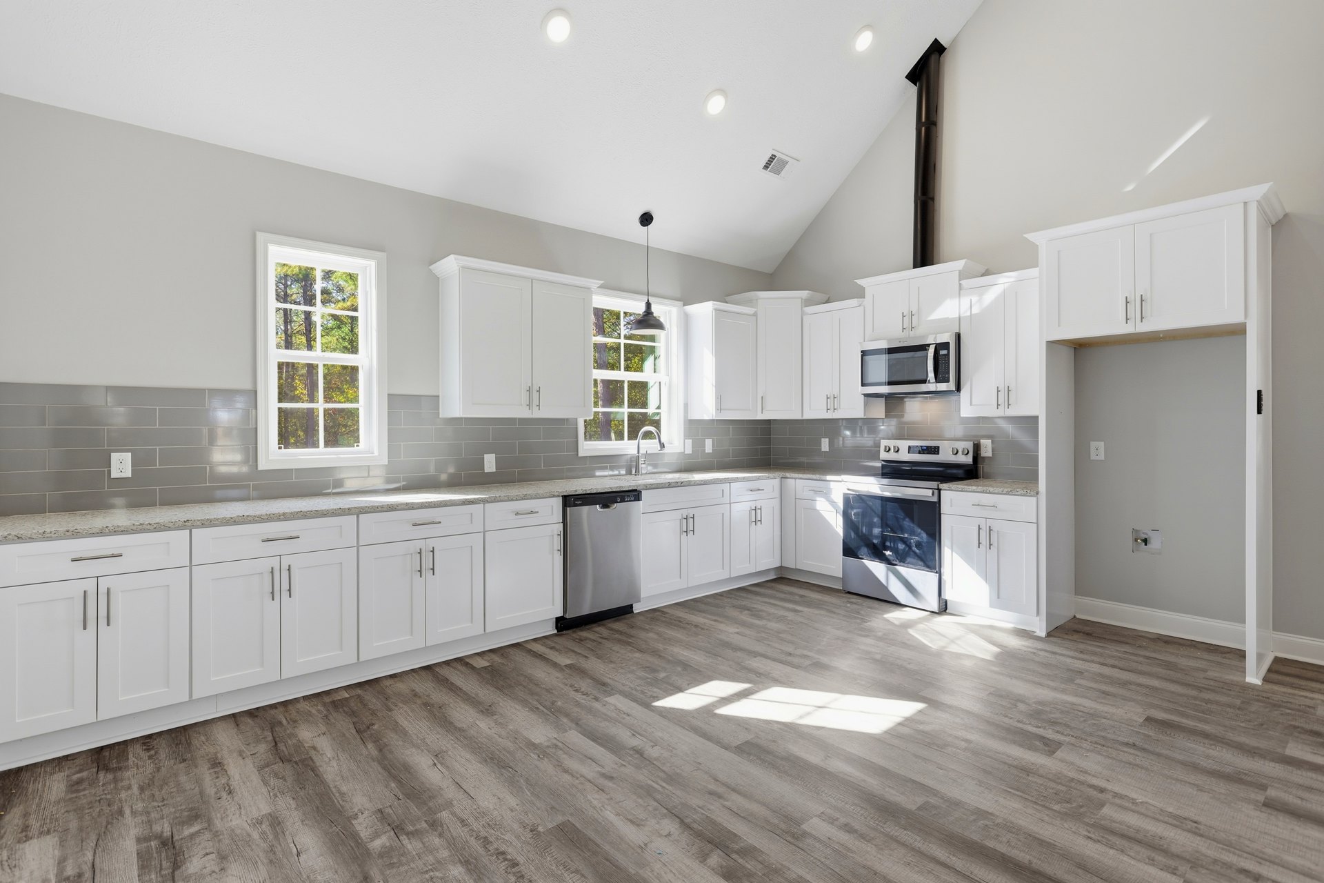 White kitchen cabinets, wood flooring, stainless steel dishwasher, open microwave, refrigerator, stove, window with trees visible outside