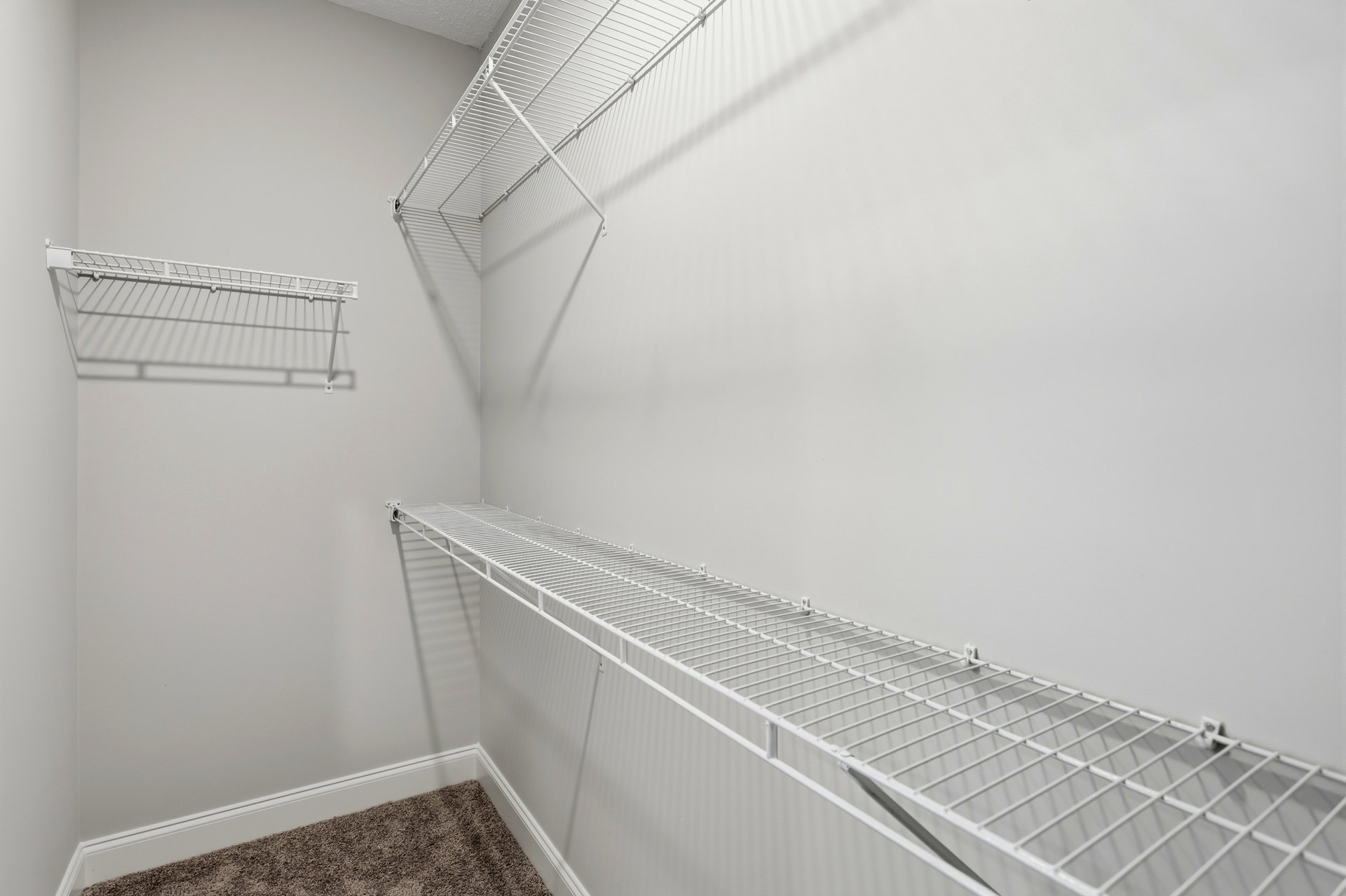 White wire shelving mounted on a plaster wall above light-colored carpet in a residential room.