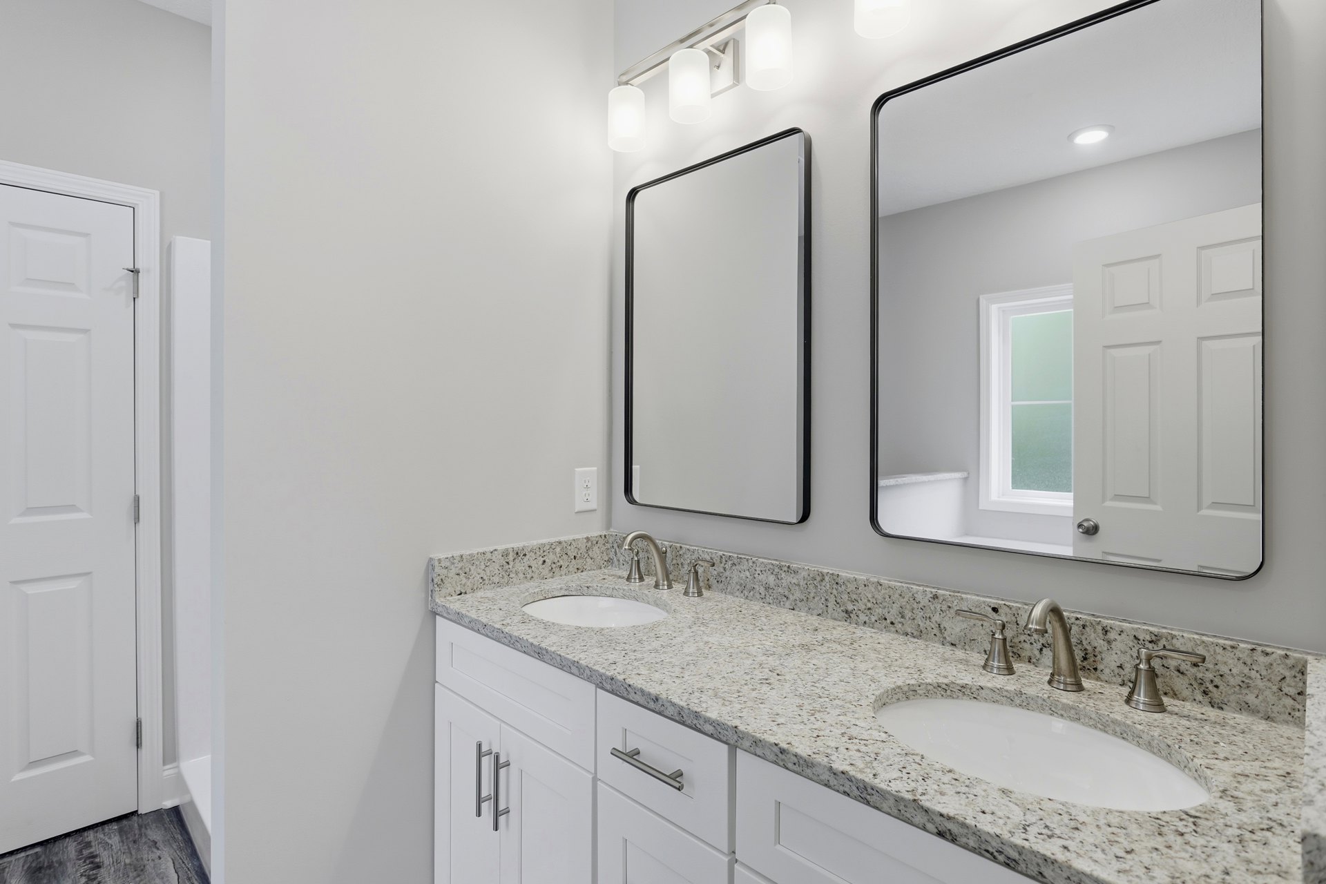Bathroom with double sinks, black-framed mirrors, white walls, white cabinetry, chrome faucets, and a white door with silver hinges
