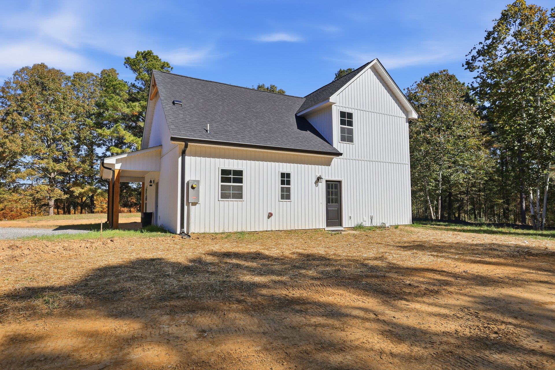 White house with black roof, surrounded by trees, grassy lawn in foreground, white-framed windows and door visible