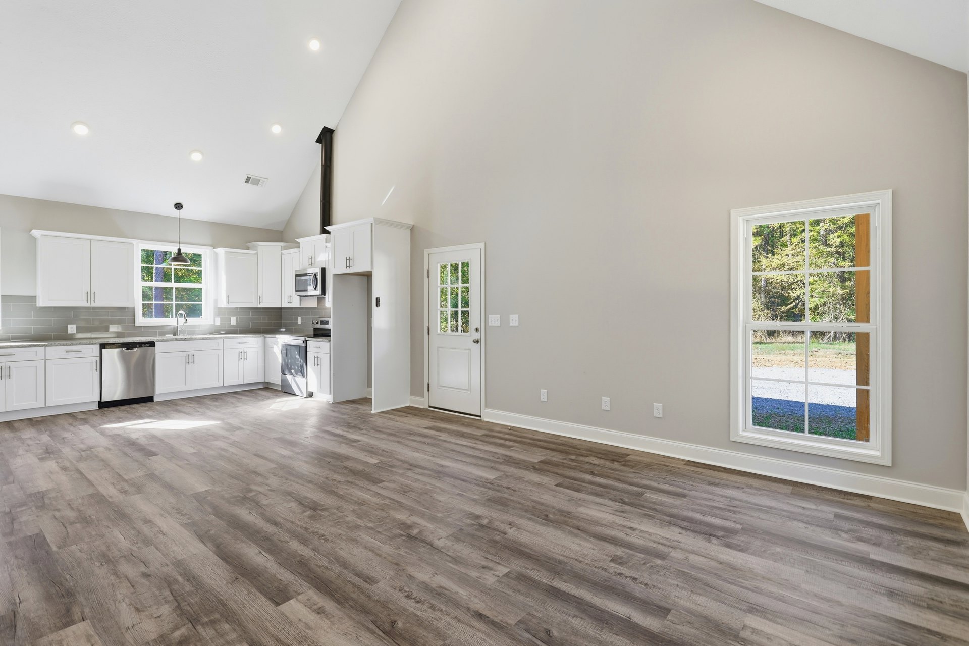 Spacious room with hardwood flooring, white cabinetry, glass-paneled door, built-in microwave, and large window overlooking forest