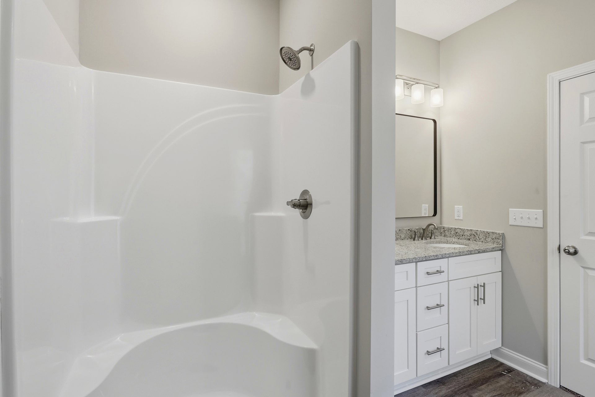 Modern bathroom featuring a glass-enclosed shower with chrome fixtures, white ceramic sink set in a wood vanity, large wall mirror, and light gray tile walls.