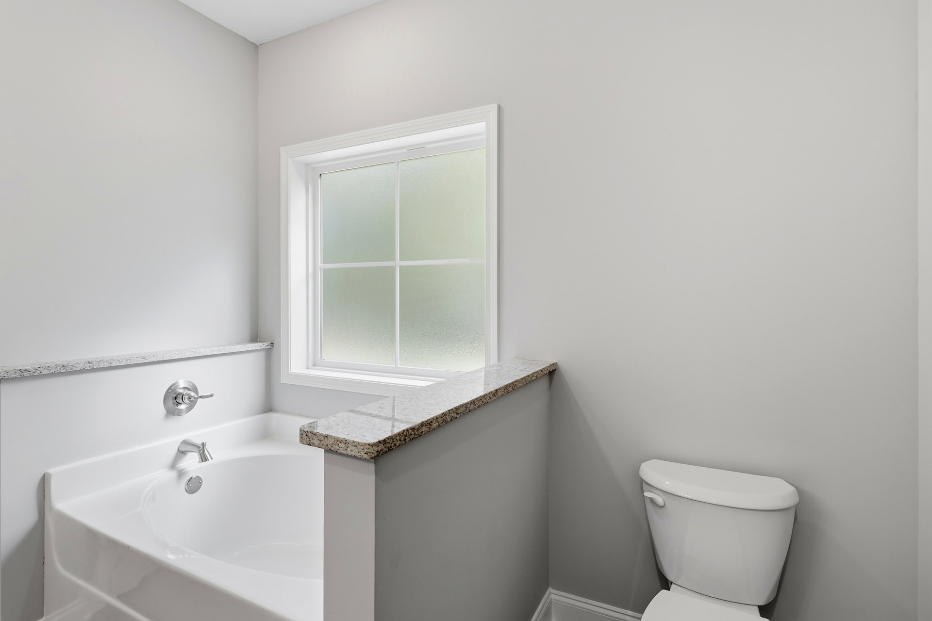 Bathroom with white bathtub and chrome faucet, white toilet with silver handle, frosted glass window, tiled walls, and light-colored countertop