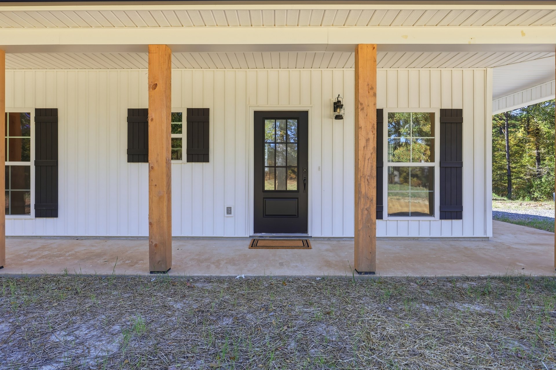 Black front door with glass panes, white siding, wooden porch post, grass and mulch landscaping