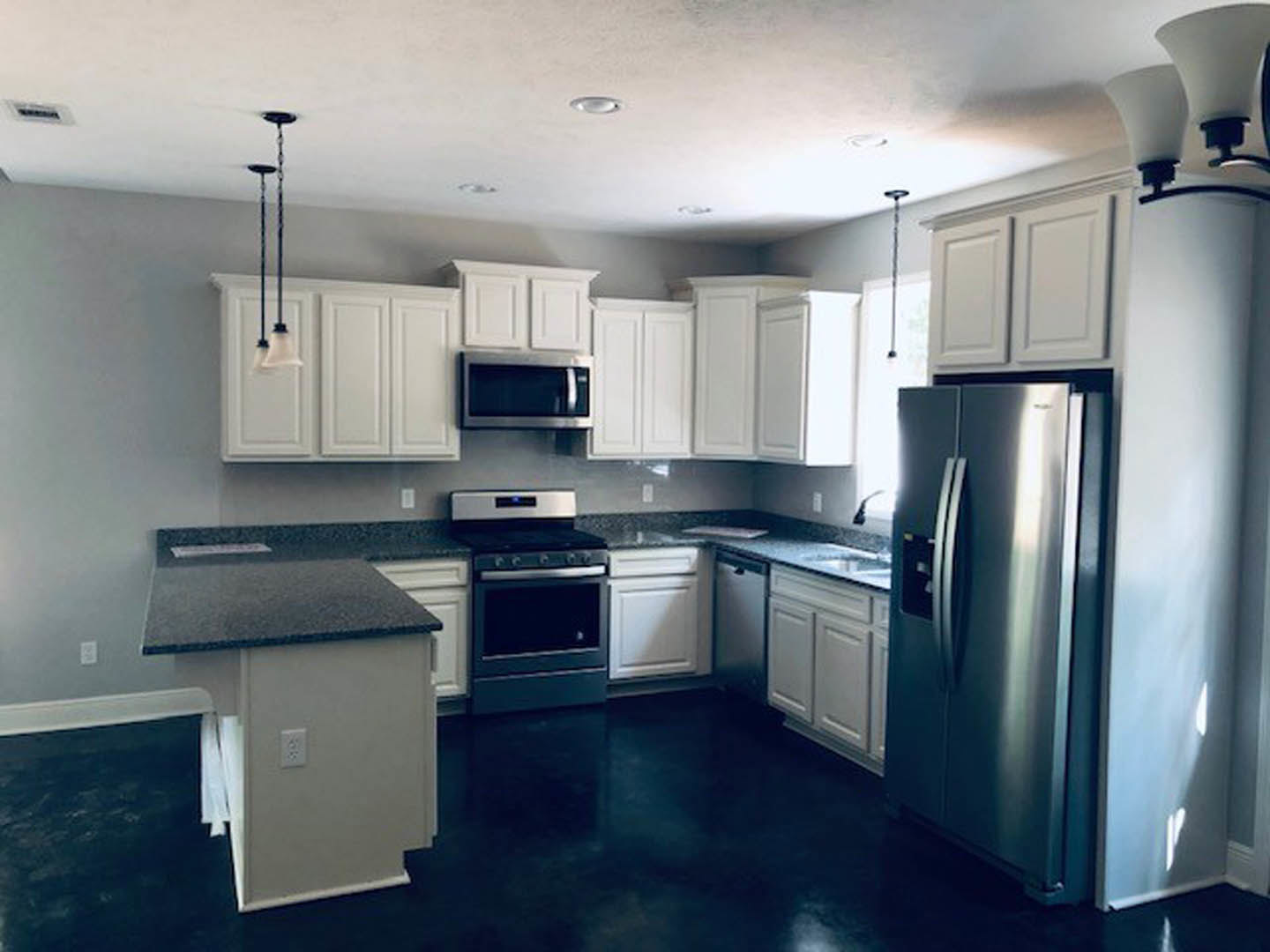 White cabinetry and black countertops in a modern kitchen with stainless steel appliances and a tile backsplash