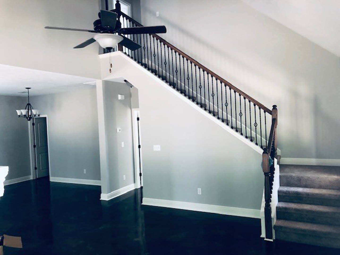 Ceiling fan with light fixture above plaster staircase, metal handrail, and shadow cast on wall