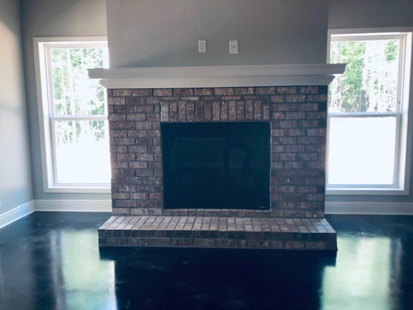 Brick fireplace with black-framed window, white walls, hardwood floor, and built-in shelves in a cozy living room