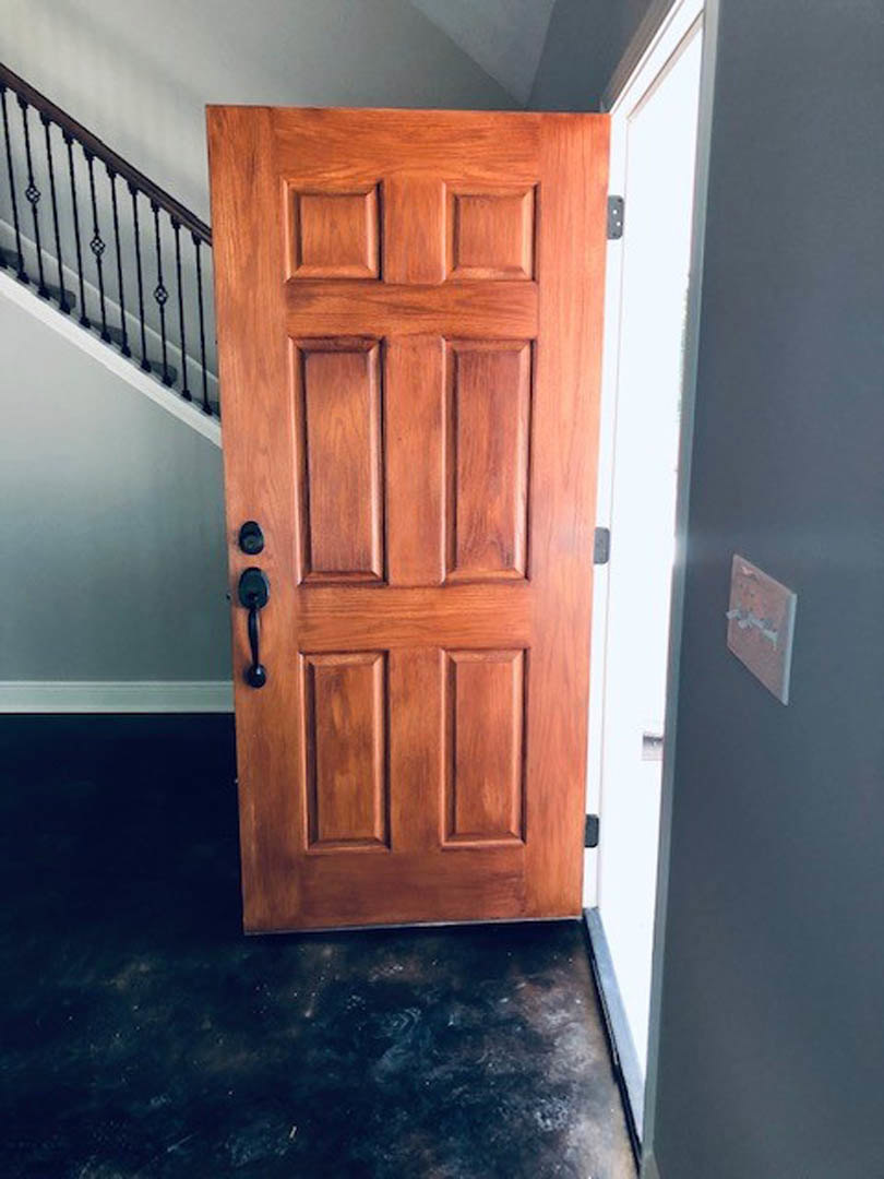 Wooden interior door with metal handle, light switch on adjacent white wall, hardwood flooring