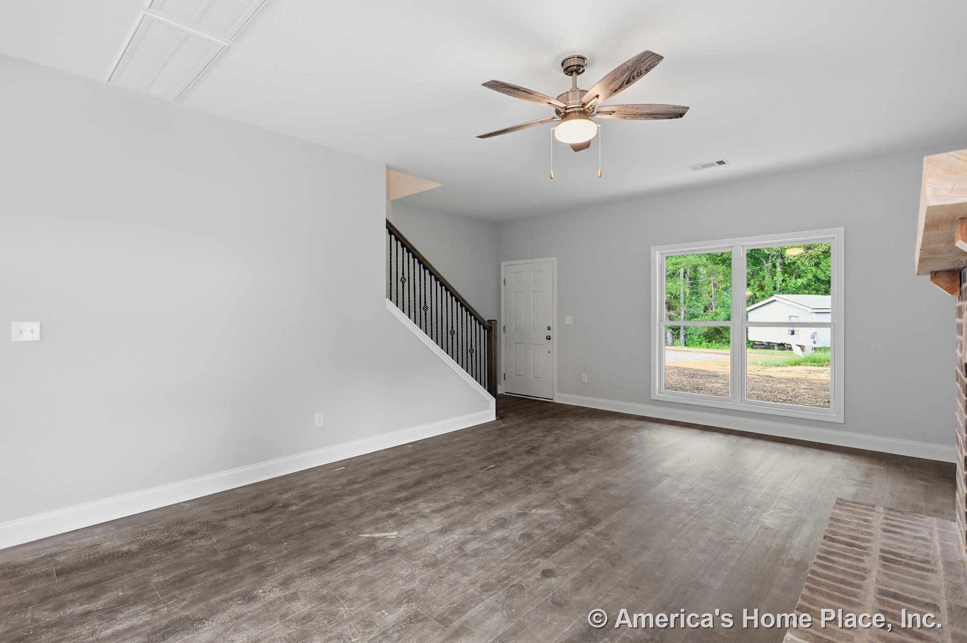 Wood-look plank flooring, ceiling fan with integrated light, large double window with white trim and baseboards, iron stair railing, brick fireplace hearth, neutral wall color