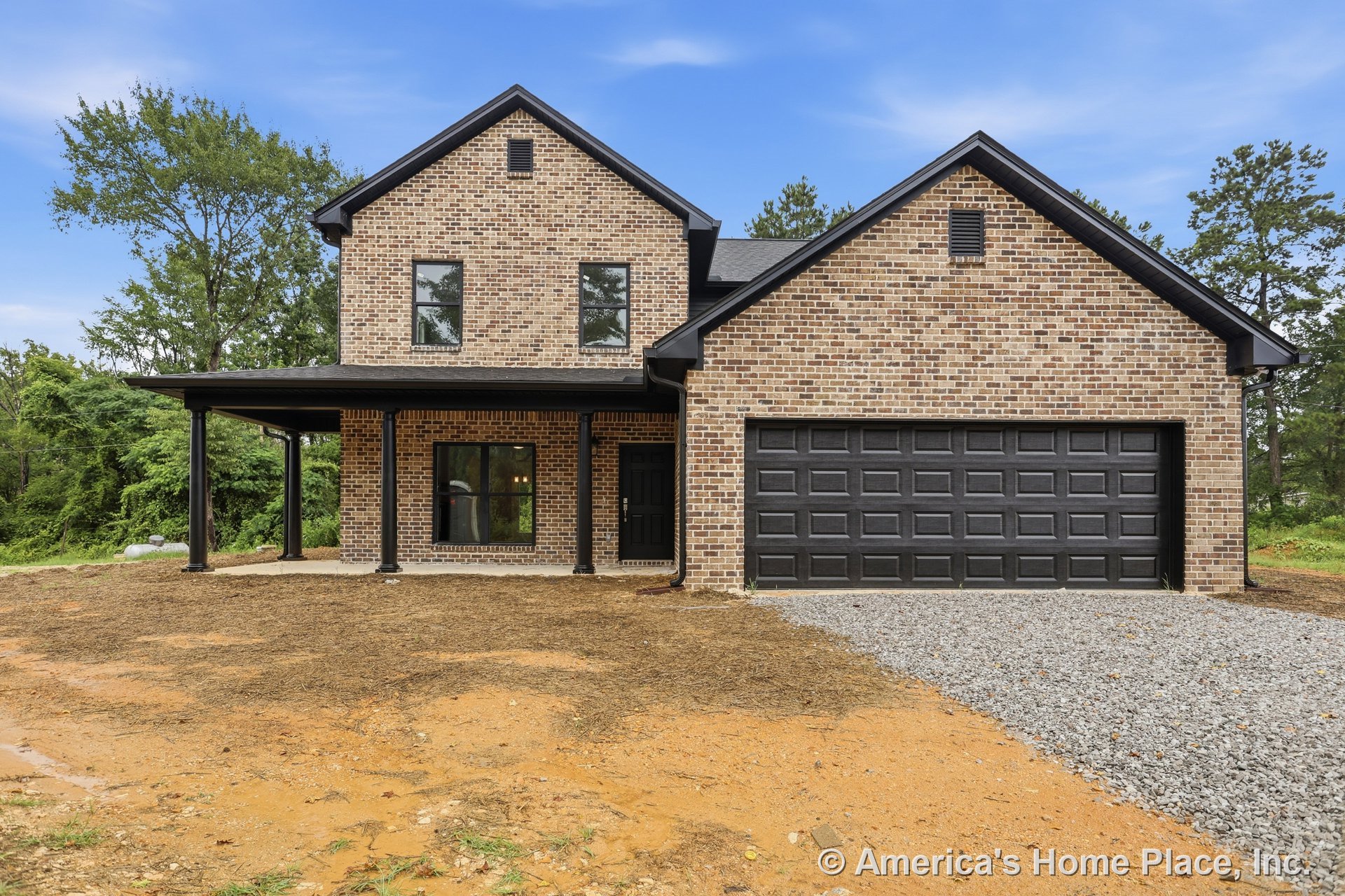 Two-story brick exterior with black framed windows, black trim, and a gabled roof; covered front porch supported by black columns; black garage door and entry door; gravel driveway