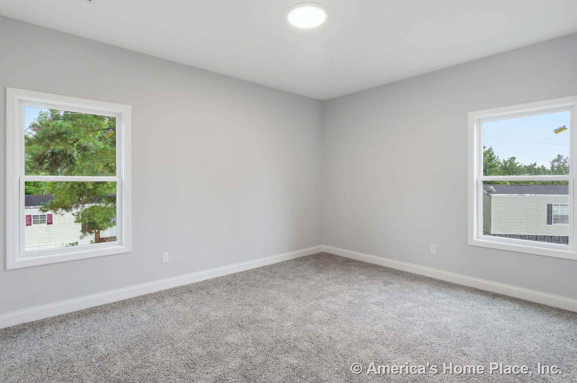 Bedroom with two large windows, light gray walls, plush gray carpet flooring, white baseboards, recessed ceiling light, and abundant natural light in a modern, neutral interior.