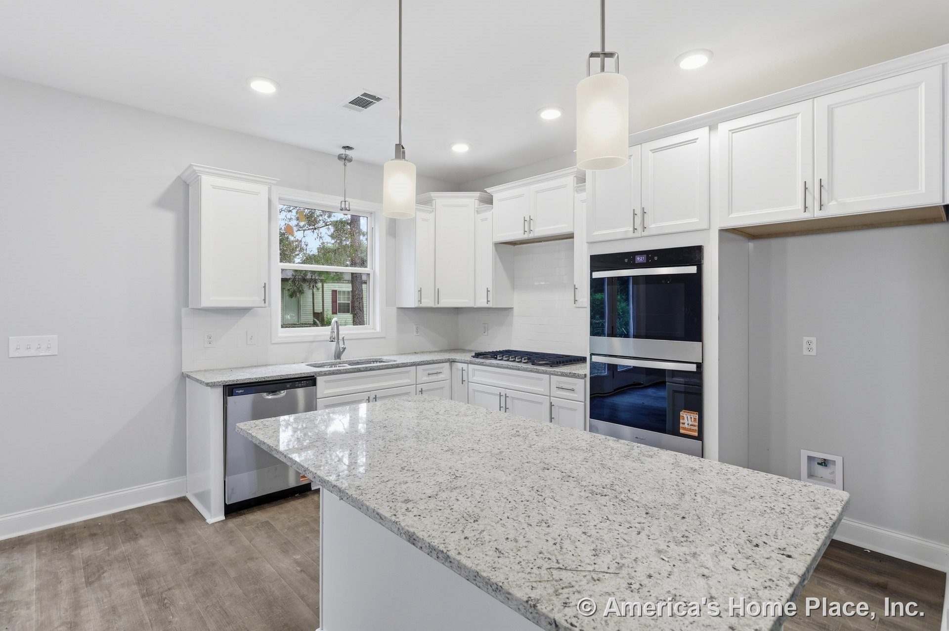 White cabinetry and granite countertops surround a central island with wood-look flooring; built-in stainless steel double wall oven, gas cooktop with vent hood, tile backsplash