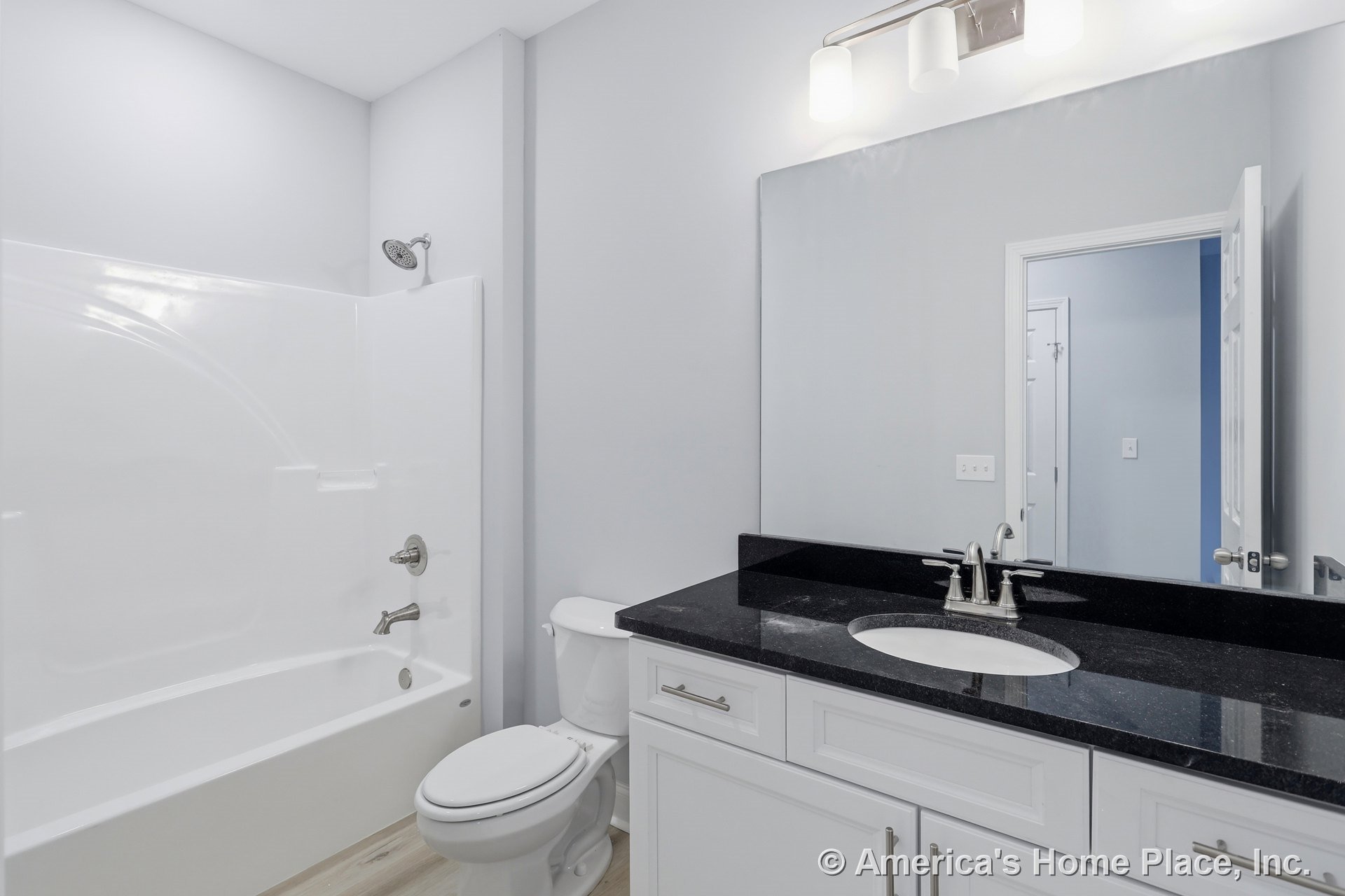 White shaker-style vanity with black granite countertop, single undermount sink, large wall mirror, modern vanity light fixture, fiberglass tub-shower combo, light wood-look