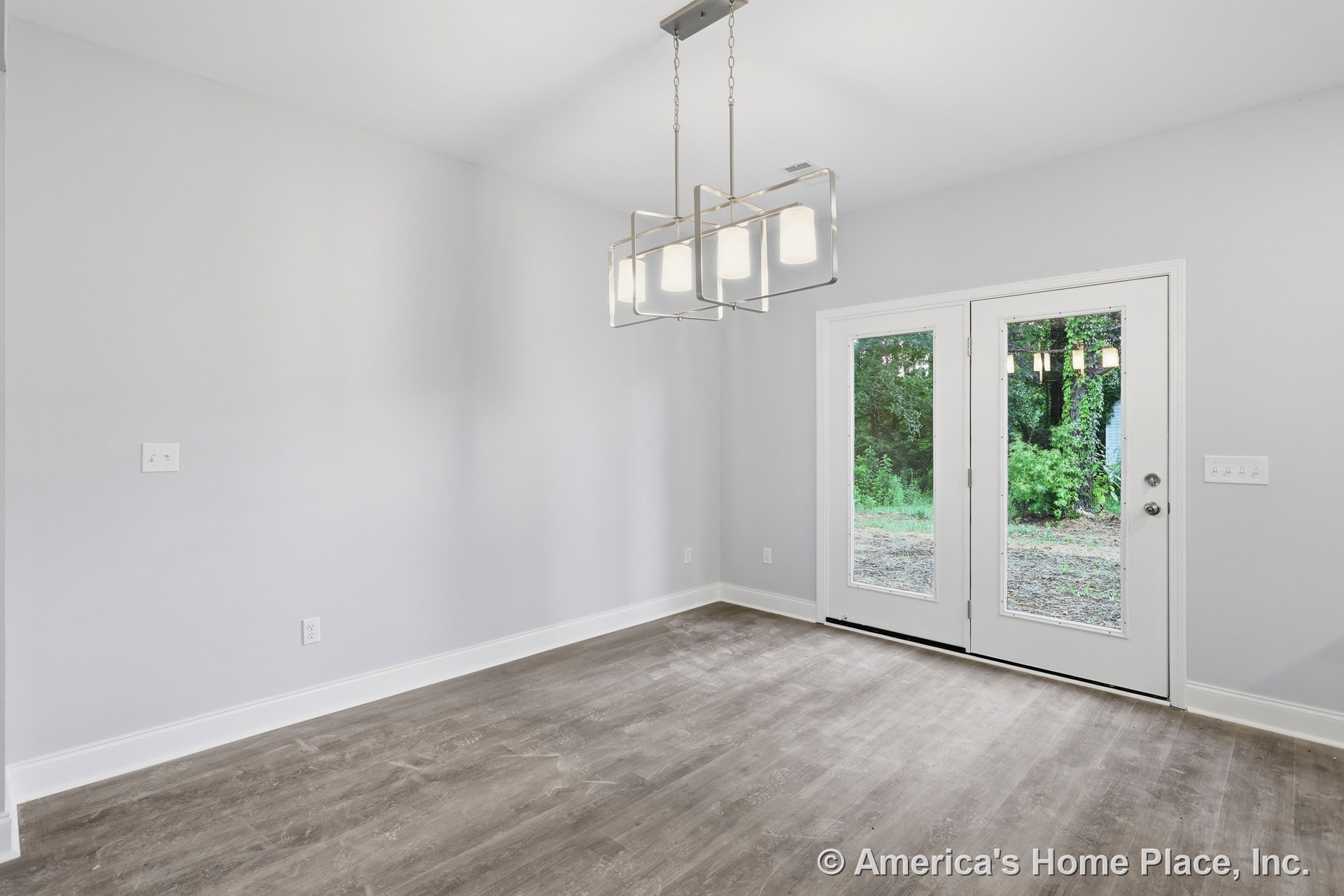 Dining area with double glass doors, modern pendant light fixture, wood-look vinyl flooring, white baseboards, light gray walls, and ceiling-mounted electrical outlets.