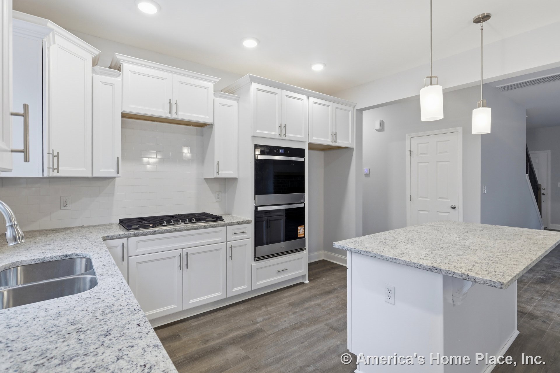 White shaker cabinets with granite countertops, double wall oven, tile backsplash, pendant and recessed lighting, central island with sink, wood-look flooring, and detailed trim.
